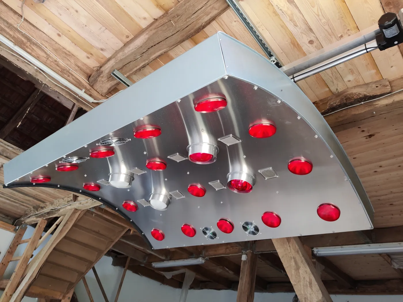 Solaride Profi am Lift in einem Holzstall, schräg von unten: gewölbte Edelstahlschale mit roten Infrarotstrahlern und Lüftern.